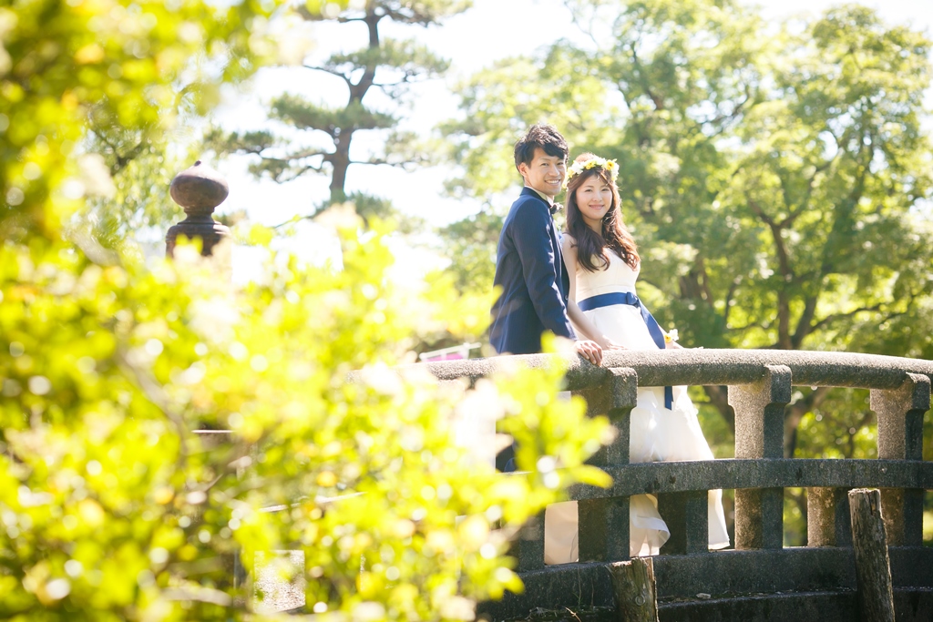 鶴舞公園の緑と橋の前でかわいい結婚写真を撮影中のふたり