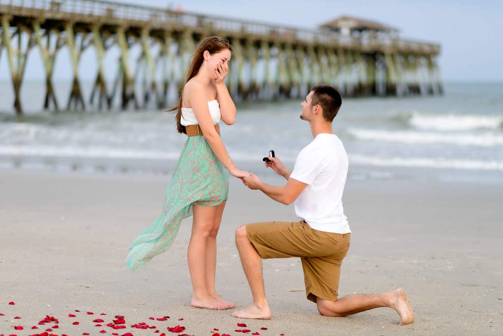 彼女の片手を握って、もう片方の手に婚約指輪を持ってプロポーズしている彼