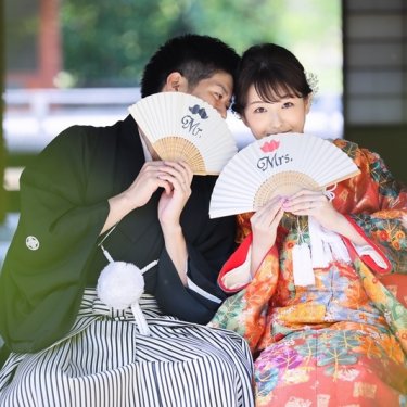 MrとMrsの扇子で顔を隠して笑う紋付袴の新郎と色打掛の花嫁。白鳥庭園で撮る大人の和装前撮りの小物