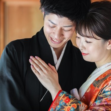 結婚指輪をはめた手を胸に添えて寄り添う紋付袴の新郎と色打掛の花嫁のアップ。白鳥庭園の和装前撮り