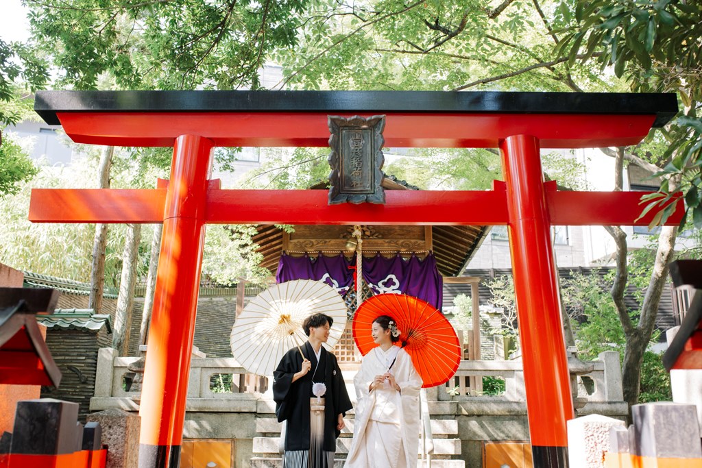 鳥居の下で和傘をさし見つめ合う新郎新婦