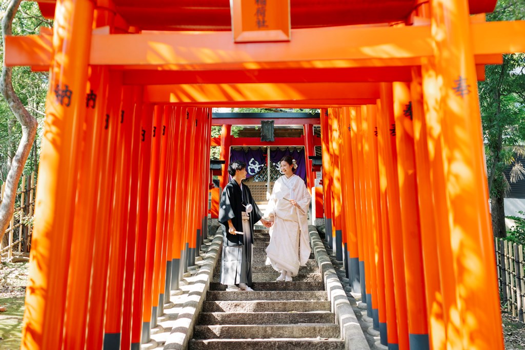 鳥居の綱らる階段で手をつないで歩く新郎新婦