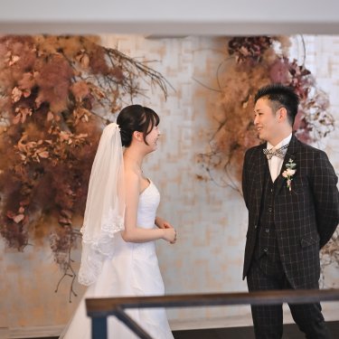 ドライフラワーの壁の前で新郎に振り返ってもらうベール姿の花嫁。スタジオ前撮りのファーストミート