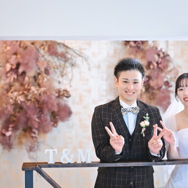 イニシャルの飾りの前でピースサインをする新郎新婦。アトリエスタジオで撮るフォトウェディング