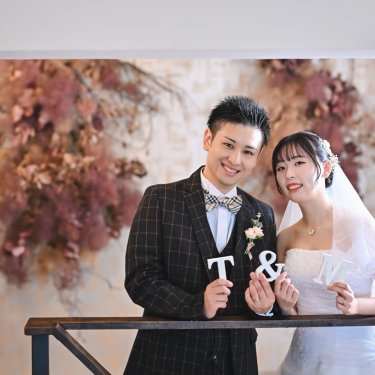 イニシャルと&のオブジェを持って笑うチェックのタキシードの新郎とベールの花嫁。アトリエの前撮りの小物