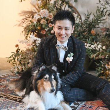 ラグの上で愛犬のコリーと座るチェックのタキシードの新郎。アトリエスタジオの前撮り