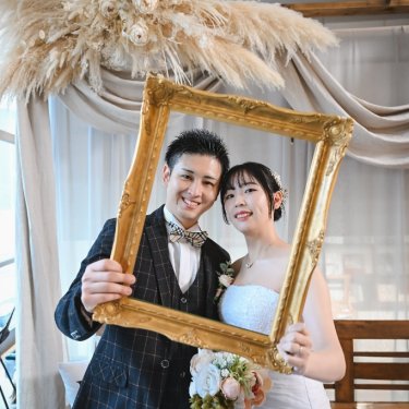 金の額縁の中で頬を寄せて笑うチェックのタキシードの新郎とウェディングドレスの花嫁。アトリエの前撮り