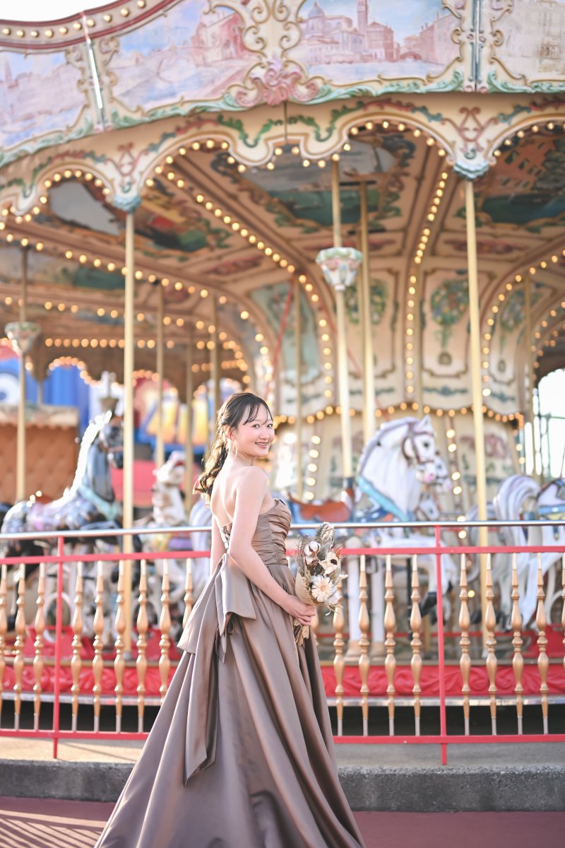 メリーゴーランドの前で振り返るカラードレスの花嫁。背中の大きなリボンが映えるシートレインランドの夜の前撮り