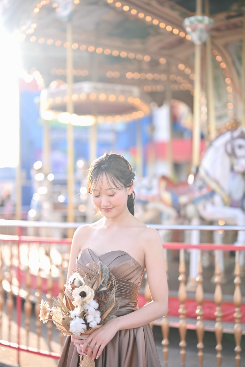 ドライフラワーのブーケを胸に目を伏せるカラードレスの花嫁。メリーゴーランドの光をぼかした名古屋のソロカット