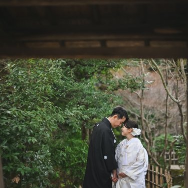 門の木枠越しに見える庭で、おでこを寄せ合う新郎新婦。額縁のような構図の東山荘での和装前撮り