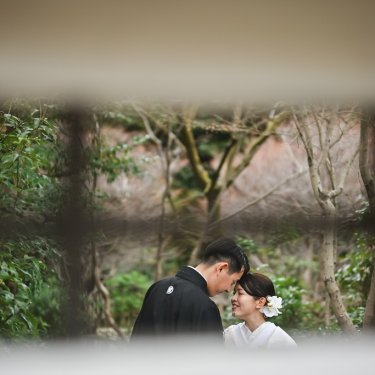 木の格子越しにのぞく、おでこを寄せる紋付袴の新郎と白無垢の花嫁。前ボケを生かした和装前撮り