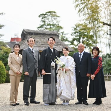 茅葺の門と松を背景に並ぶ白無垢の花嫁と紋付袴の新郎とご家族。和装前撮りに合わせて撮影した家族写真