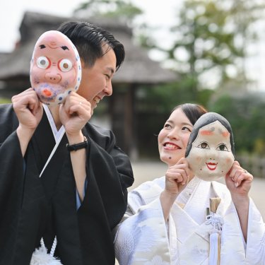 おかめとひょっとこのお面を手に笑う白無垢の花嫁と紋付袴の新郎。遊び心のある和装前撮りの小物使い