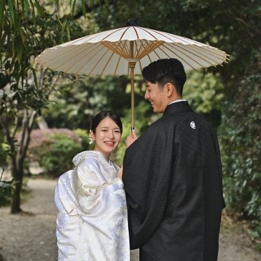 竹垣のある庭で白い和傘を差し、振り返って笑う白無垢の花嫁と紋付袴の新郎。東山荘の庭で撮る和装前撮り