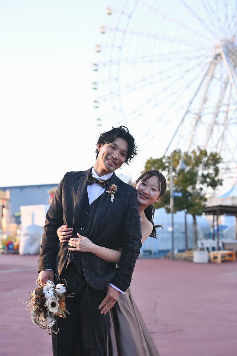 大観覧車を背に新郎の腕に寄り添ってほほえむブラウンのカラードレスの花嫁。名古屋港シートレインランドの洋装前撮り