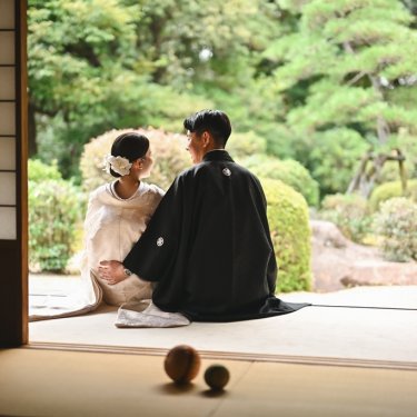 手入れされた日本庭園を前に、東山荘の縁側に並んで座る白無垢の花嫁と紋付袴の新郎。静かな和装ロケーションフォト