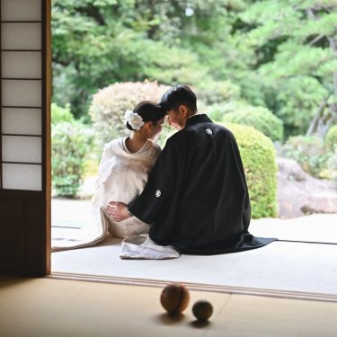 日本庭園を望む縁側に座り、おでこを寄せ合う新郎新婦の後ろ姿。手まりを置いた和装前撮りの構図