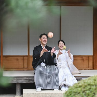 縁側に腰かけ、手まりを投げて笑う紋付袴の新郎と白無垢の花嫁。東山荘の庭で撮る遊び心のある和装前撮り