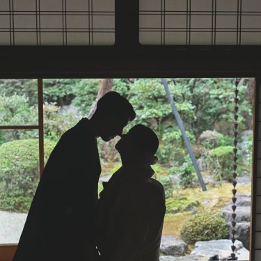 庭へ開いた窓辺で、おでこを寄せ合う新郎新婦のシルエット。緑の日本庭園が浮かぶ和装前撮り