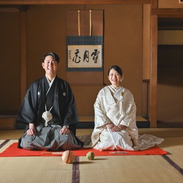 掛け軸のある和室で、緋毛氈の上にそろって座り笑顔を見せる新郎新婦。東山荘の座敷で撮る和装フォトウェディング