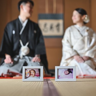 ふたりの赤ちゃんの頃の写真を手前に置き、和室に並んで座る紋付袴の新郎と白無垢の花嫁。家族への感謝を込めた前撮り