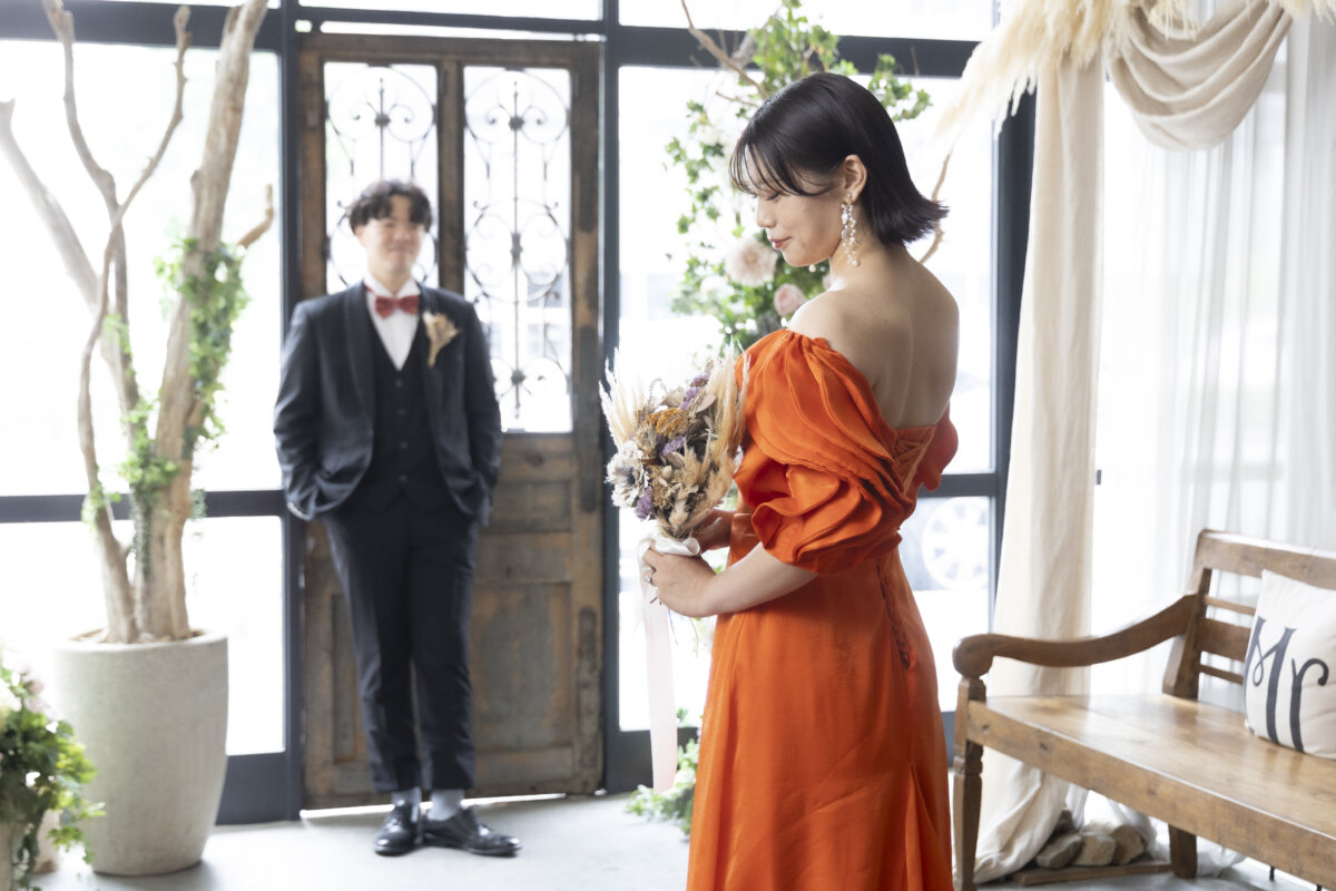 アンティークの扉の前に立つ新郎と、背中の編み上げを見せるオレンジのカラードレスの花嫁。名古屋のアトリエスタジオで撮る洋装前撮り