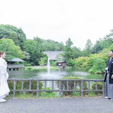 噴水と池のある庭園を背に、離れて立ち見つめ合う新郎新婦。広い景色を生かした和装フォトウェディング
