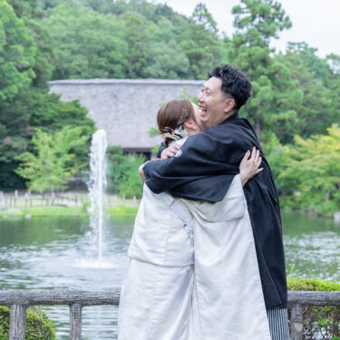 噴水のある池を背景に、抱き合って喜ぶ白無垢の花嫁と紋付袴の新郎。宗節庵で撮った和装ロケーションフォト