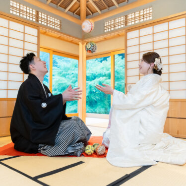 赤い毛氈を敷いた茶室で、手まりを投げ上げて遊ぶ紋付袴の新郎と白無垢の花嫁。宗節庵の和室で撮った和装前撮り