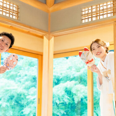 障子の陰から狐のお面とひょっとこのお面を手に顔を出す新郎新婦。茶室で撮る遊び心ある和装前撮り