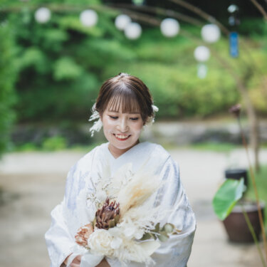 提灯のアーチの下で、ドライフラワーのブーケを手に微笑む白無垢の花嫁。白鳥庭園の緑に映える和装の結婚写真