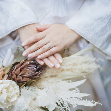 結婚指輪をつけた手を重ね、パンパスグラスとドライフラワーのブーケを添えた白無垢の花嫁の手元。和装前撮りのアイテムカット