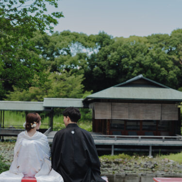 白鳥庭園の池のほとりで赤い縁台に腰かけ、茶室を眺める新郎新婦の後ろ姿を写した結婚写真