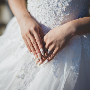ビジューのウェディングドレスの前で手を重ね、結婚指輪を見せる花嫁の手元アップ。洋装前撮りのディテールカット