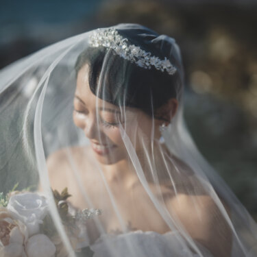 ロングベールをかぶりブーケを持って微笑む、ティアラの花嫁のアップ。やわらかな光で撮るベールショットの前撮り