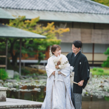 池と和風の建物を背に、新郎を見上げて笑う白無垢の花嫁。ドライフラワーのブーケが映える白鳥庭園でのフォトウェディング