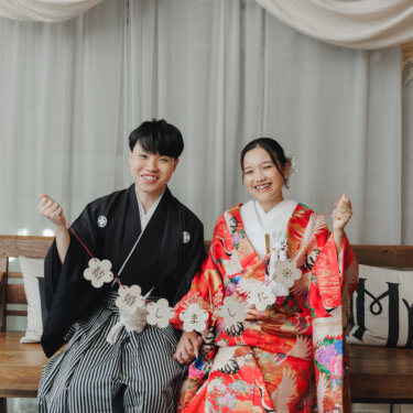 '結婚しました'のガーランドを二人で持ち、ベンチに座って笑う紋付袴の新郎と赤い色打掛の花嫁。名古屋のスタジオで撮る結婚報告にも使える前撮り