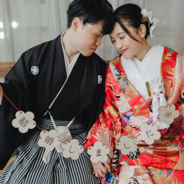 結婚しましたのガーランドを持ち、おでこを寄せ合って目を閉じる紋付袴の新郎と赤い色打掛の花嫁。和装前撮りで人気のおでこ合わせポーズ