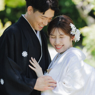 寄り添って目を細めて笑い合う紋付袴の新郎と白無垢の花嫁。白鳥庭園の木漏れ日の中で撮る和装フォトウェディング