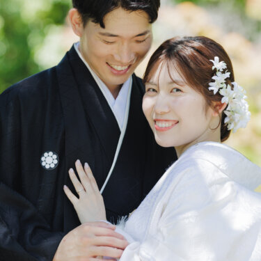 新郎の胸に手を添えてカメラに笑顔を向ける白無垢の花嫁と、やさしく抱き寄せる紋付袴の新郎の和装前撮り