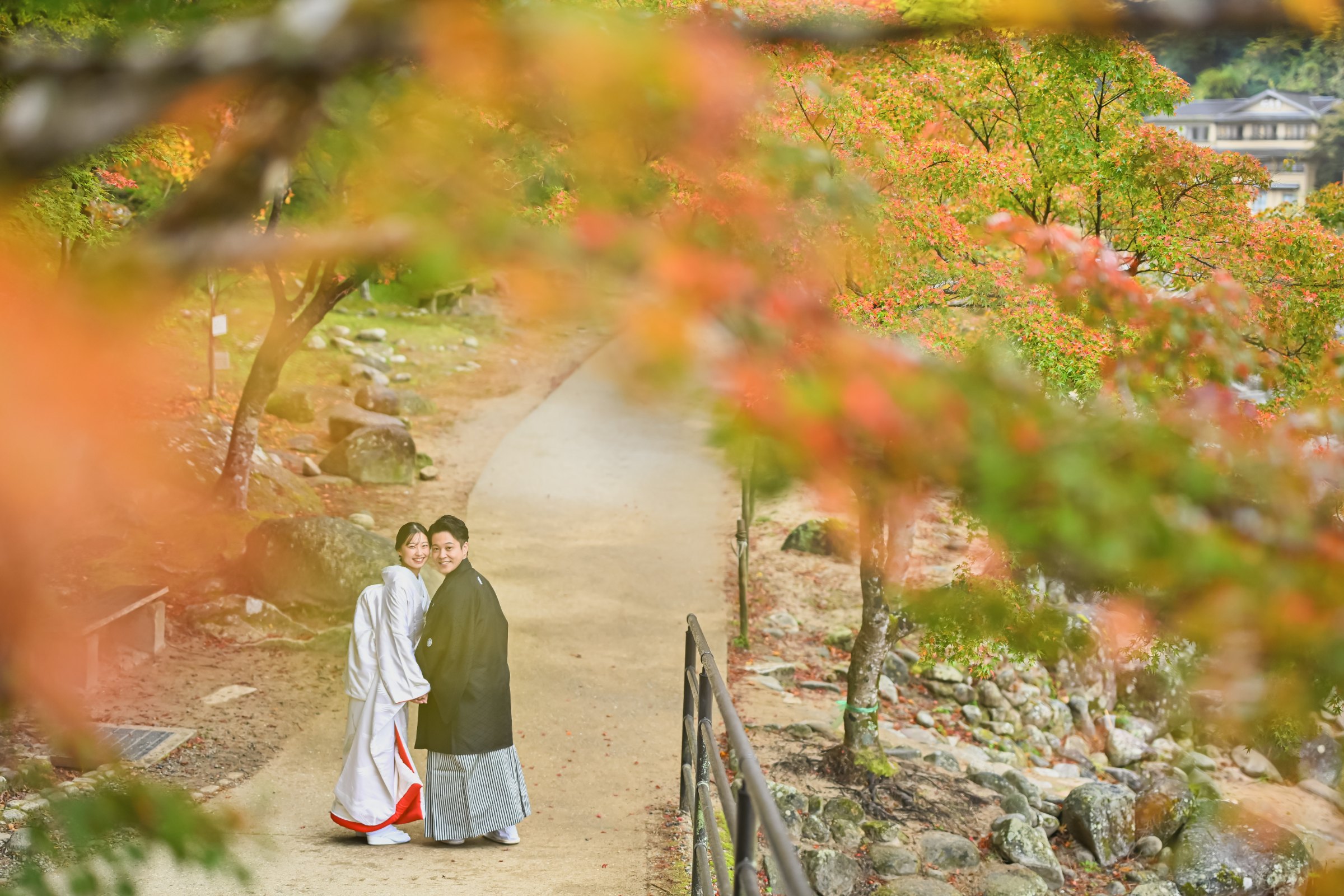 紅葉した木々を背に振り返る新郎新婦、白無垢姿の新婦と黒紋付袴の新郎、香嵐渓の山里風景。