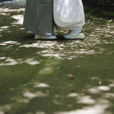 木漏れ日が落ちる庭園の小道で、寄り添って立つ新郎新婦の袴と白無垢の足元を写した和装ロケーションフォト
