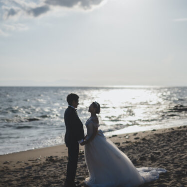 夕方の光がきらめく海辺の砂浜で、向かい合って手を取る新郎新婦。知多半島で撮るロマンチックなビーチ前撮り