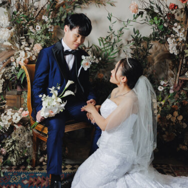 アンティークの椅子に座るタキシードの新郎の膝に手を添え、床に座って見上げるベール姿の花嫁。名古屋のアトリエスタジオで撮るウェディングフォト