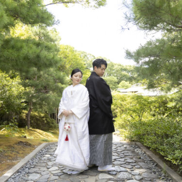 松に囲まれた石畳の小道に並んで立つ、白無垢の花嫁と紋付袴の新郎。白鳥庭園で撮る和装ロケーションフォト