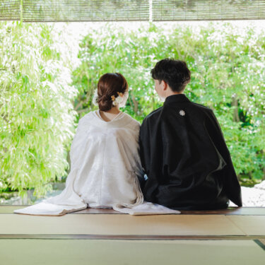 竹の緑を望む茶室の縁側に並んで座る、白無垢の花嫁と紋付袴の新郎の後ろ姿を写した結婚写真