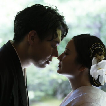 緑を背に鼻先を寄せ合う新郎新婦の横顔。胡蝶蘭と水引の髪飾りが映える白無垢の花嫁の和装前撮り