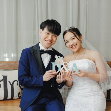Mr&Mrsのクッションのベンチに座り、イニシャルのオブジェを二人で持って笑うタキシードの新郎とウェディングドレスの花嫁。小物アイテムを使った前撮り