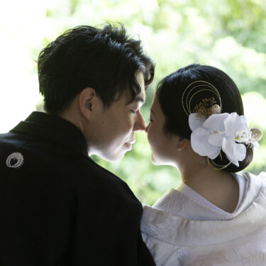 新郎の肩越しに、鼻先を寄せて見つめ合う白無垢の花嫁を写した構図。白鳥庭園で撮るロマンチックな和装前撮り