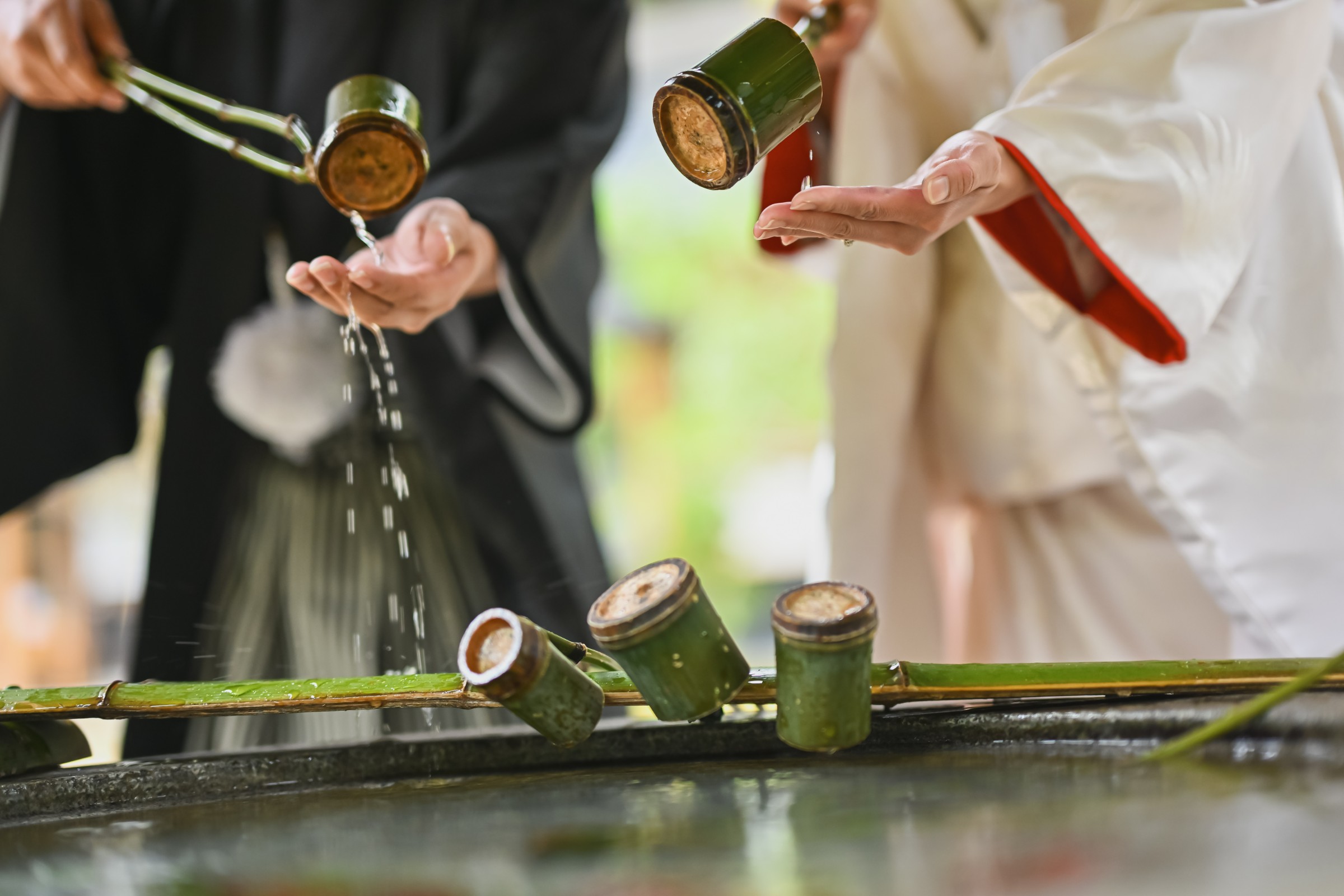 手水舎で身を清める新郎新婦、竹の柄杓で水をすくう黒紋付の新郎と白無垢姿の新婦、和装での清めの儀式。